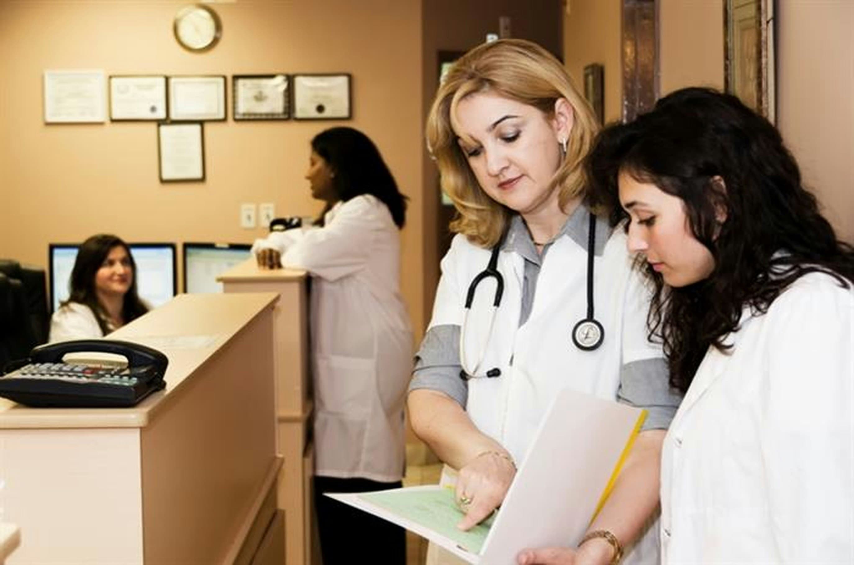 A clinic front desk with staff checking in patients and reviewing paperwork