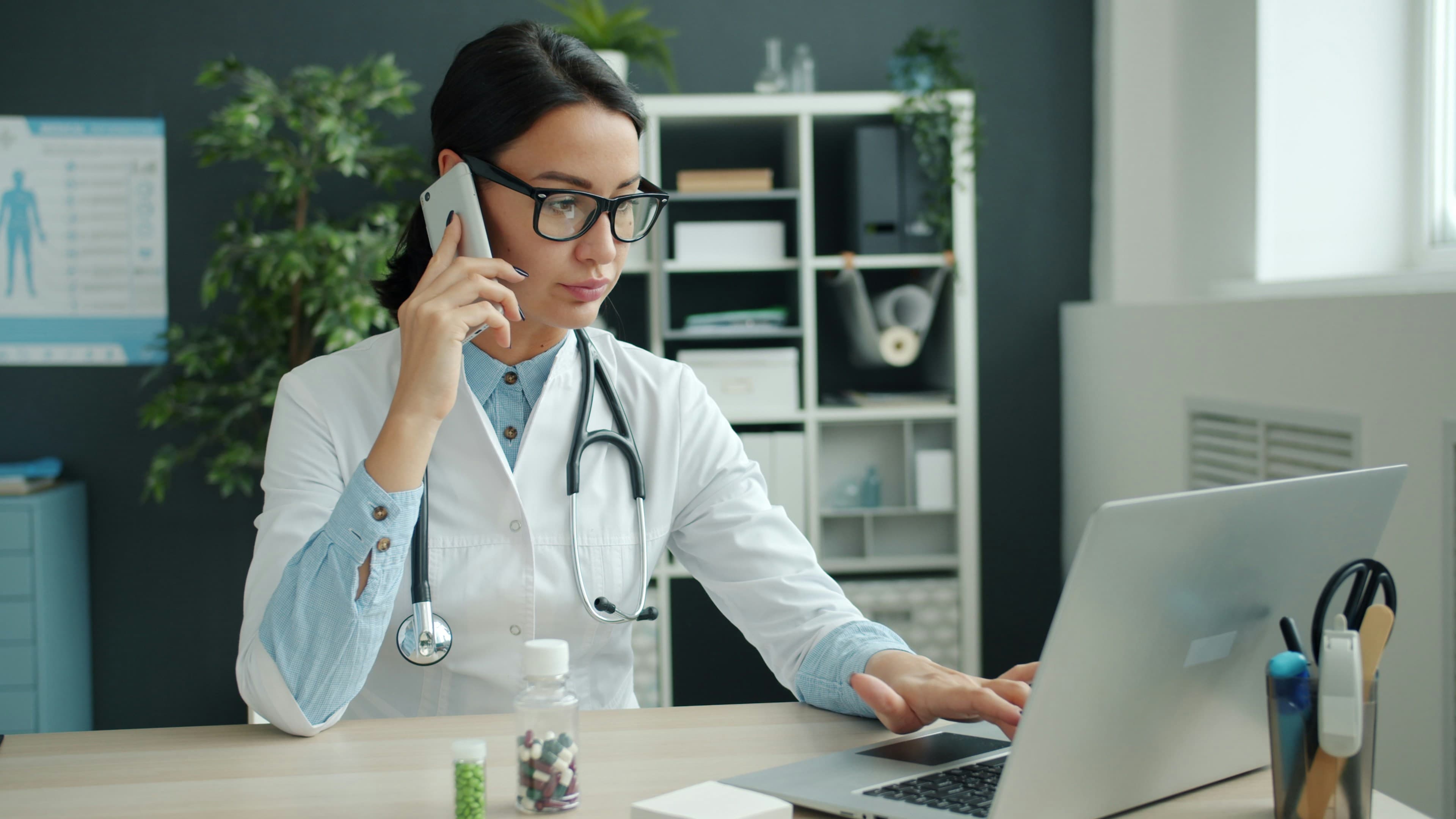 A doctor on the phone while working on a laptop